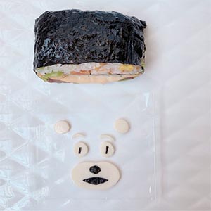 在用海苔剪出眼珠、鼻子和嘴巴,黏在起士片上後,放在飯糰上做出五官,最後擠上蕃茄醬當腮紅就完成囉!