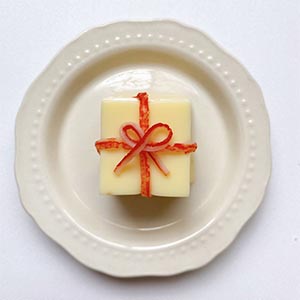 進行禮物盒的造型點綴:取一小塊切好的芙蓉豆腐,將蟳味棒剝細絲,取2條細絲擺十字在芙蓉豆腐上,再取1細絲折成蝴蝶結置中