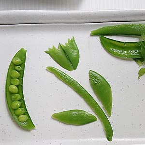 取一甜豆。撥成2瓣,將裡頭的豆子集中在其中一瓣做為裝飾用。
其餘依圖示,用食物剪剪成花托、花梗、花瓣、葉子,剩下的甜豆則切細絲與步驟2-1的沙拉拌在一起。