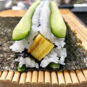 鋪一張海苔在底部,並放上兩條黃瓜醋飯置底,再放上一條玉子燒,再放上最後兩條黃瓜醋飯。