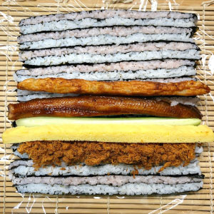 底下鋪上壽司簾與保鮮膜,將醋飯條「立著」鋪上,放入炸貝魚漿、肉鬆、玉子燒、蒲燒鰻等食材。